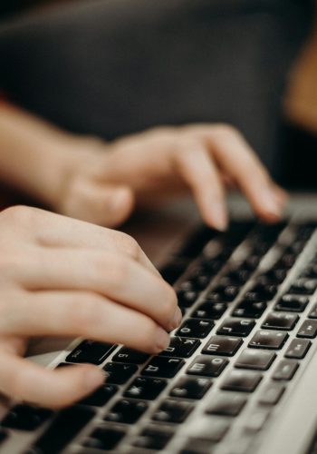 Close-up shot of hands typing on a laptop keyboard in a work environment.