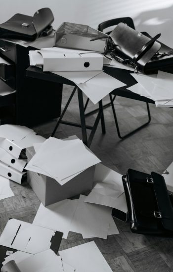 A chaotic office desk covered with scattered papers, folders, and a briefcase.